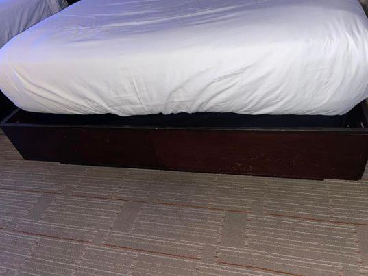 Hard Rock Hotel & Casino Biloxi Exterior photo The photo shows a bed with a white mattress and bedsheet. The bed frame is dark-colored wood, and there is a storage compartment or drawer visible underneath the bed. The flooring appears to be a patterned carpet. The overall setting seems to be a be