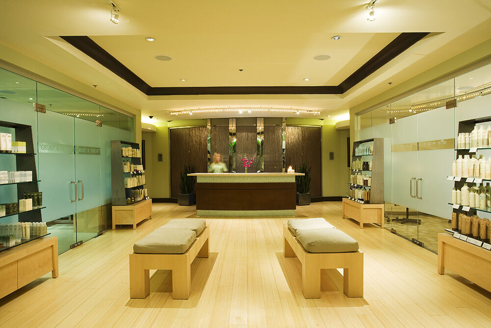 Hard Rock Hotel & Casino Biloxi Exterior photo The photo shows the interior of a spa or wellness center. In the foreground, there are two wooden benches for seating. In the background, there is a reception area with a wooden front desk, where staff members can be seen. The walls have a modern des